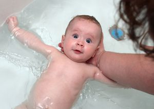 Женщина начала мыть голову новорожденному в ванне.